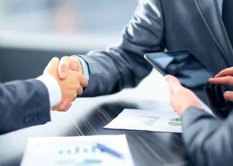 Business professionals shaking hands over a tablet, discussing IT solutions.