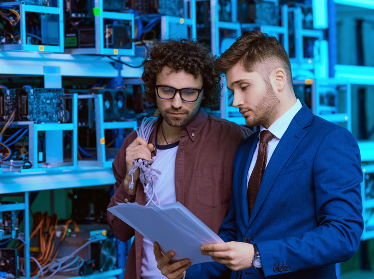Two men in a server room discussing IT management costs.