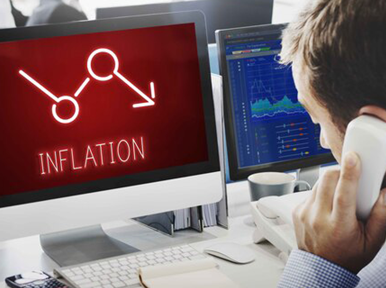 Man on phone at desk with computer monitor showing inflation symbol