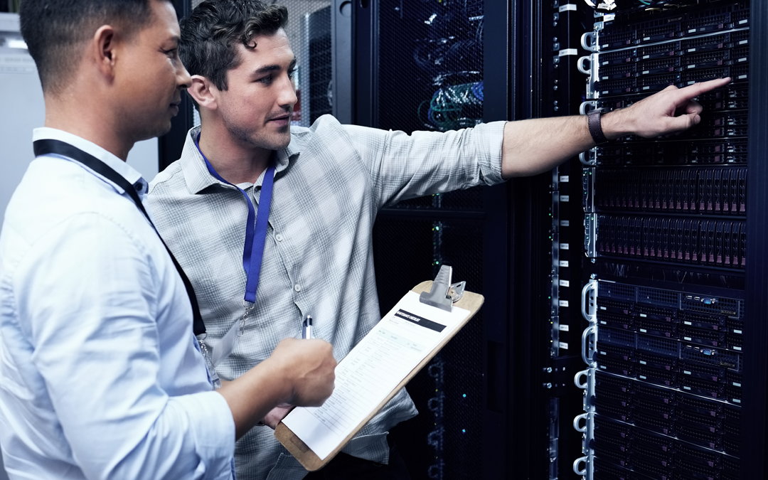 Two men in a server room, one pointing at the servers, the other holding a clipboard