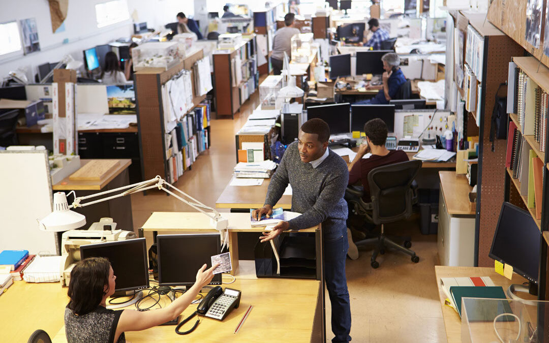 Office workers using computers; one man standing at a desk