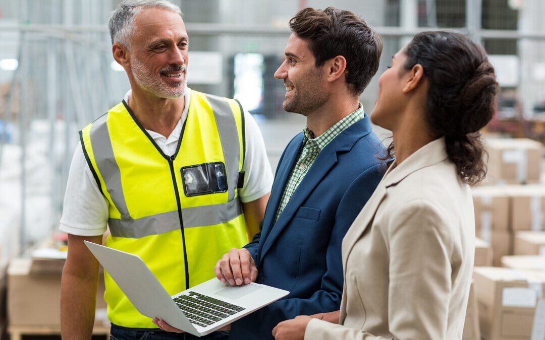 Warehouse team discusses IT management on laptop, highlighting business success.